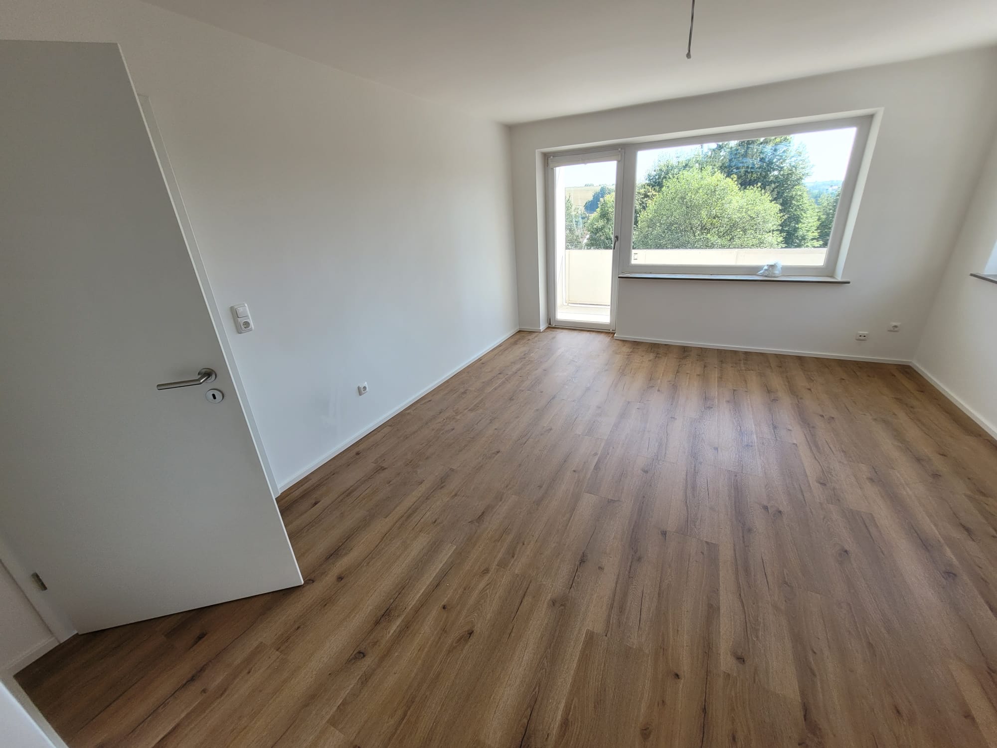 Dasselbe Wohnzimmer nach der Renovierung: weiße Wände und Decke, Boden in Holzoptik, Blick ins Grüne